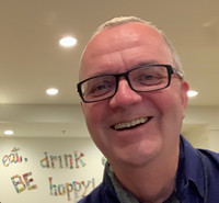 Photo of Ingo Cornils smiling in front of a wall that says: "Eat, drink, and be happy!"