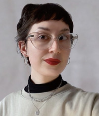 Portrait of Eva Zirker: Her dark brown hair is in a bun. She is wearing expressive glasses and red lipstick